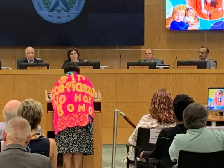 Houston ISD parent Jessica Campos, while wearing a crocheted shawl that says, “Sin confianza no hay bono,” speaks to the district’s board of managers on Thursday, Aug. 8, 2024. Adam Zuvanich/Houston Public Media