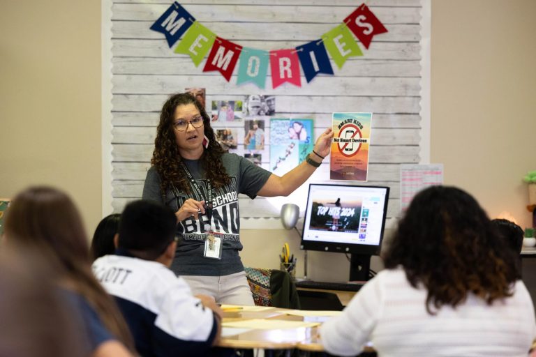 Sixth grade English teacher Shannon Brady holds a sign explaining a ban on smart devices during the school day, at Hudson Bend Middle School on Wednesday. Photo Credit: Patricia Lim / KUT News